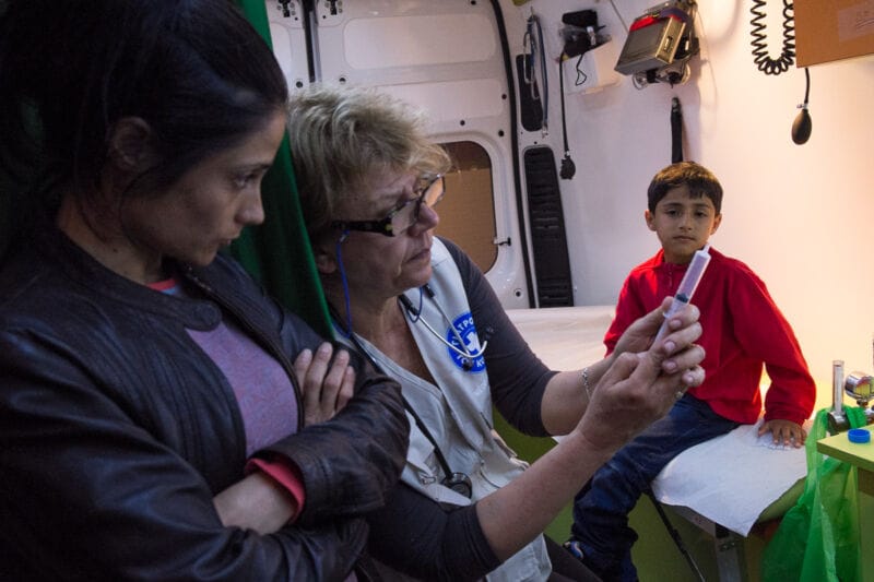 Una médica de una unidad móvil atiende a una madre y su hijo, personas refugiadas, en el puerto del Pireo en Atenas